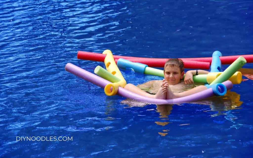 Boy in pool with pool noodles